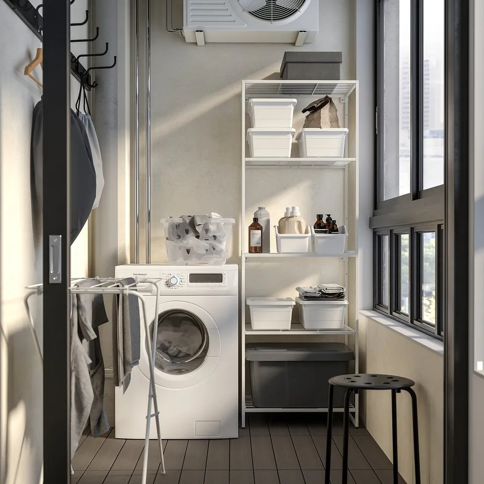Modern laundry room with white JOSTEIN washing machine, storage shelves, and clothes rack. Organised with clear containers and cleaning supplies.