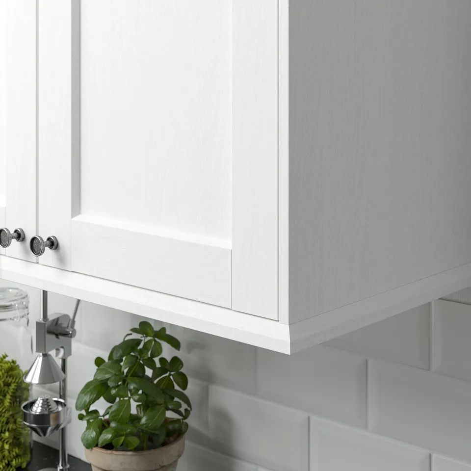 White kitchen cabinet with ENKÖPING trim, covering lighting and cords, plant on counter.