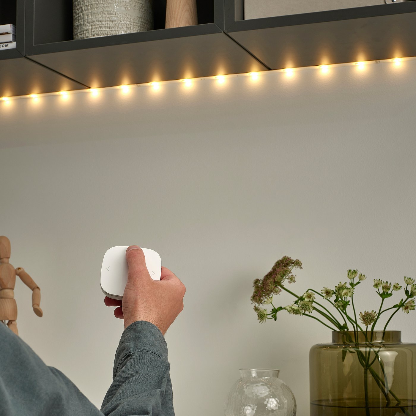 Hand holding remote, controlling led lights above cabinet.