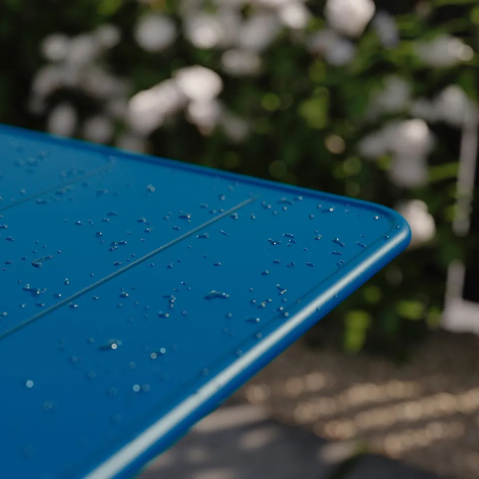 Blue folding table top with water droplets, outdoors.