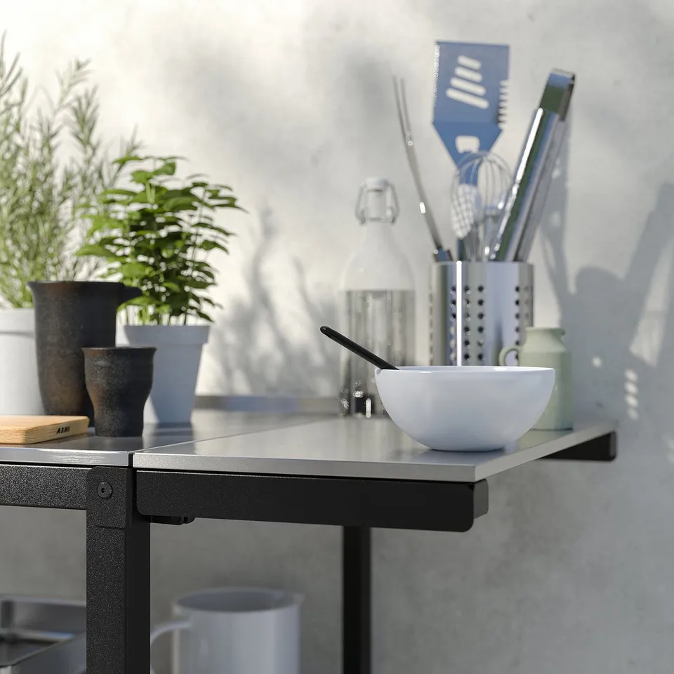 Modern kitchen scene with stainless-steel counter, white bowl, potted plants, and cooking utensils.