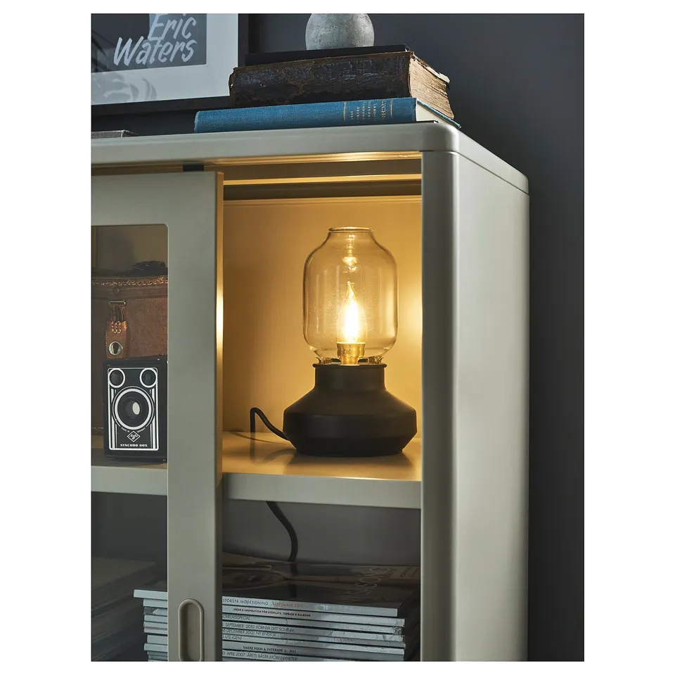 Modern silver IDÅSEN cabinet with glass doors, displaying a lit lamp and decorative items.