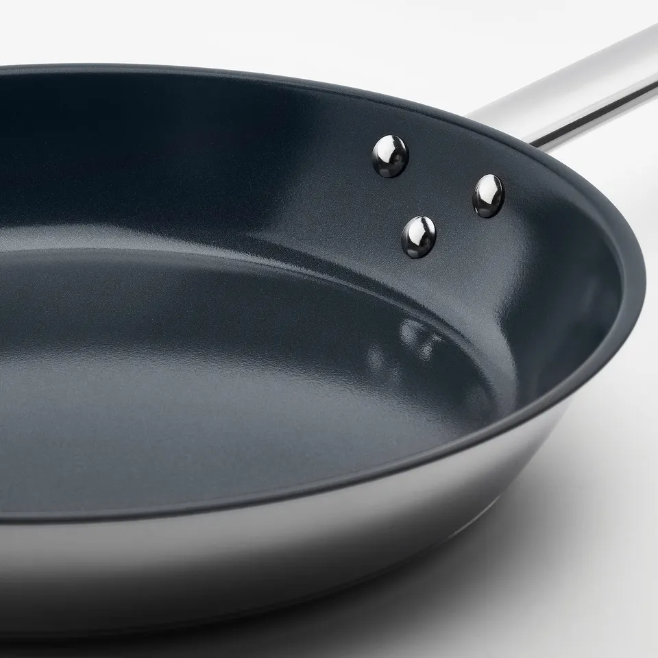 Modern frying pan with non-stick surface, shiny metal handle, and robust design, lying on a clean white surface.