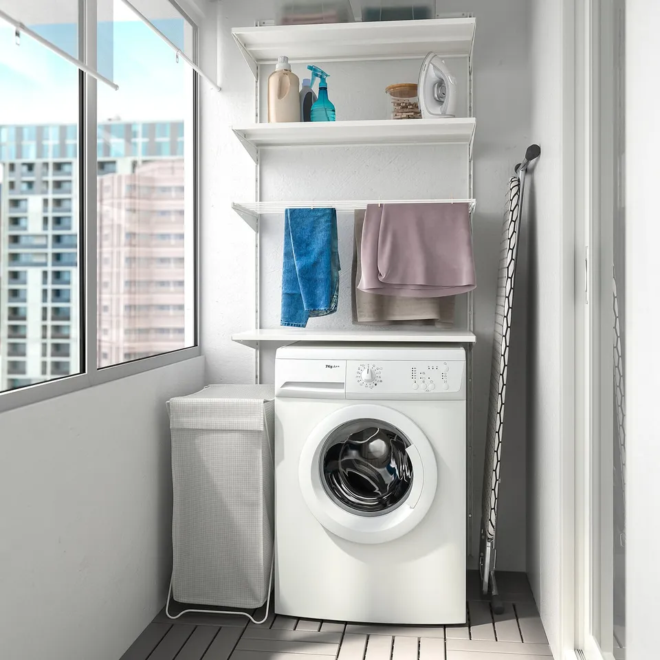 Laundry corner with white shelves, towels, machine, basket, ironing board, window.