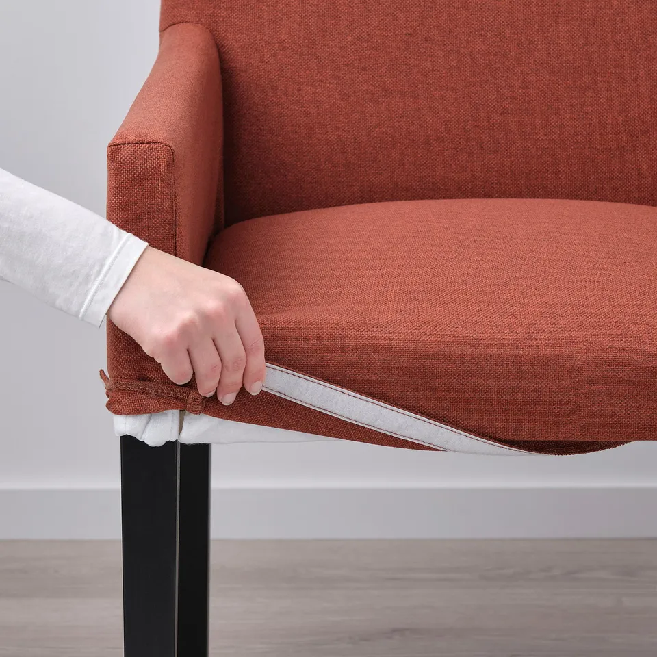 A hand adjusting a removable cover on an orange MÖRBYLÅNGA chair.