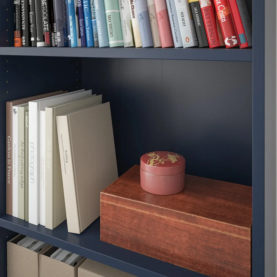 A wooden shelf unit with a dark blue frame, holding colourful books and a small decorative box.