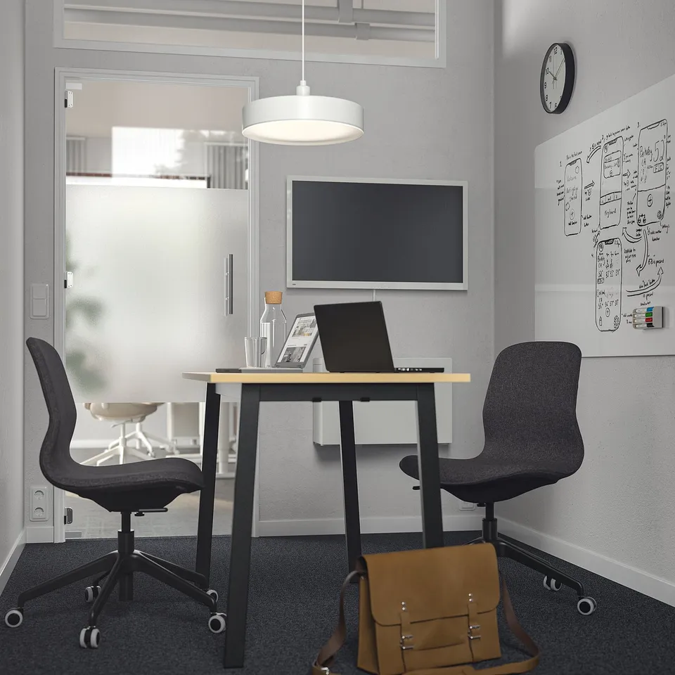 Modern office with MITTZON table, chairs, laptop, tv, clock, and bag.