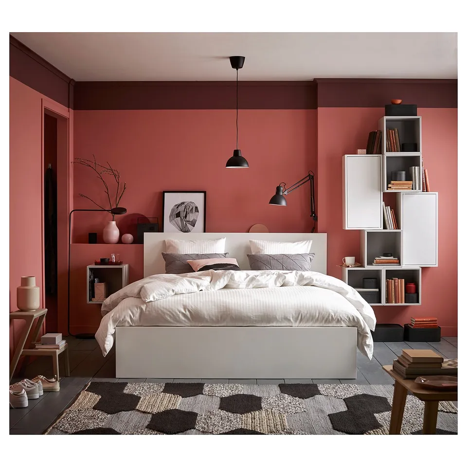 Modern rosy bedroom featuring MALM bed, white bedding, adjustable lamps, wall shelves with books, patterned rug, and minimalist decor.
