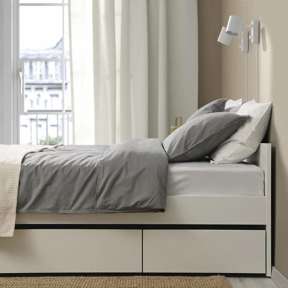 Modern bed frame with built-in storage. Grey bedding set and headboard visible. Window with city view in background.