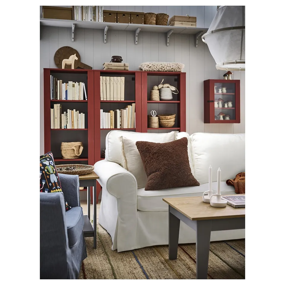 Cosy living room with white sofa, brown pillow, red bookshelf, and wooden coffee table.