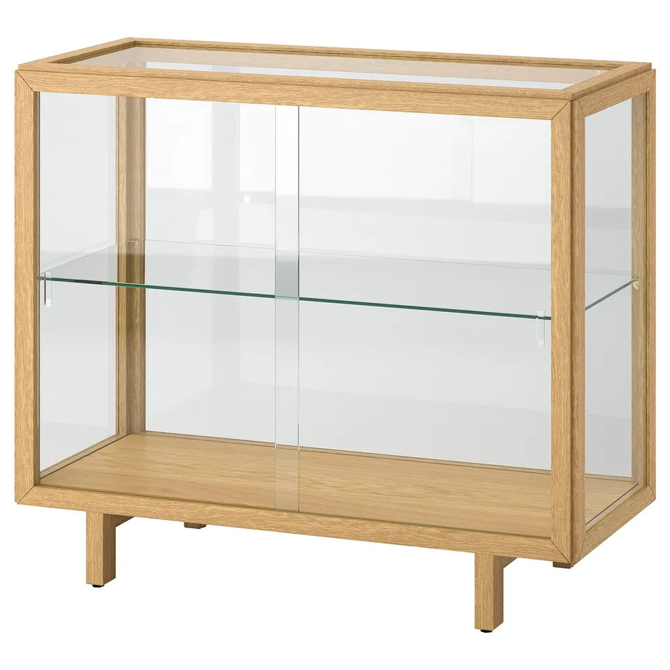A wooden and glass display cabinet, named STOCKHOLM 2025, in a light oak finish. It has clear glass doors and shelves, with a sleek, modern design.