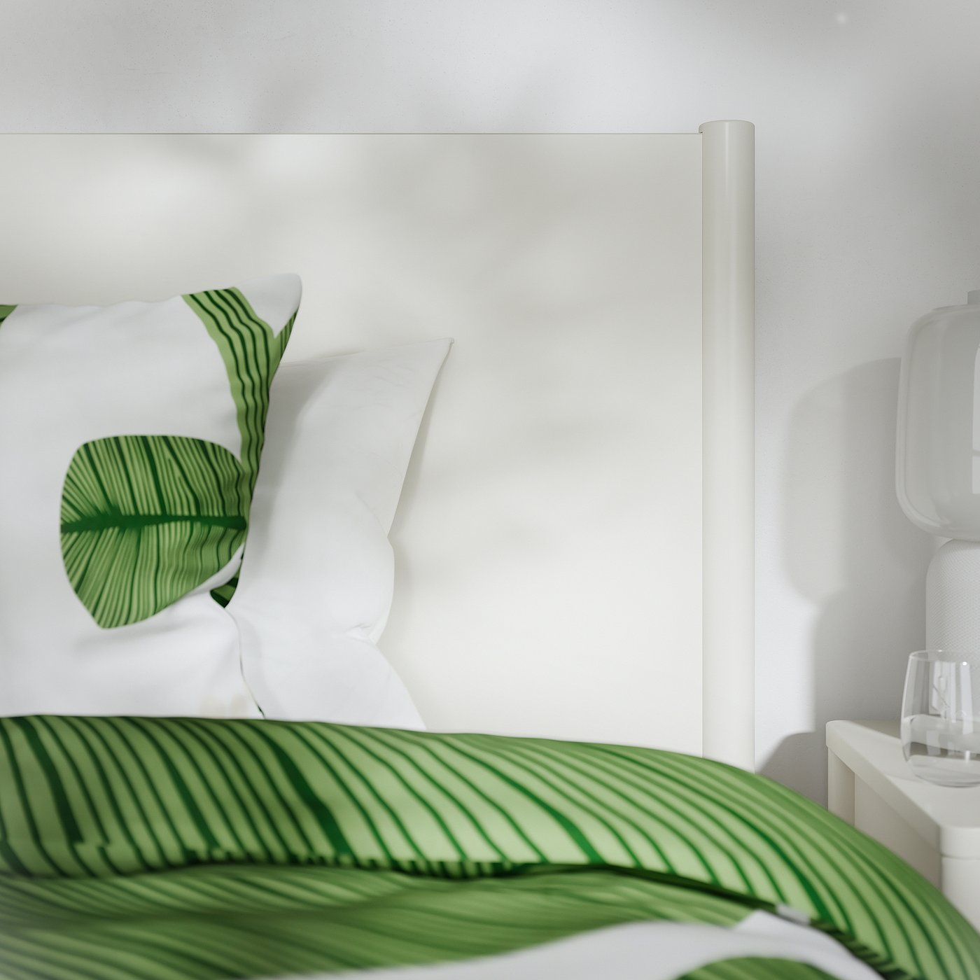 A well-made bed with a sturdy metal frame, soft pillows, and a green leaf-patterned duvet showcasing high-quality materials and design.