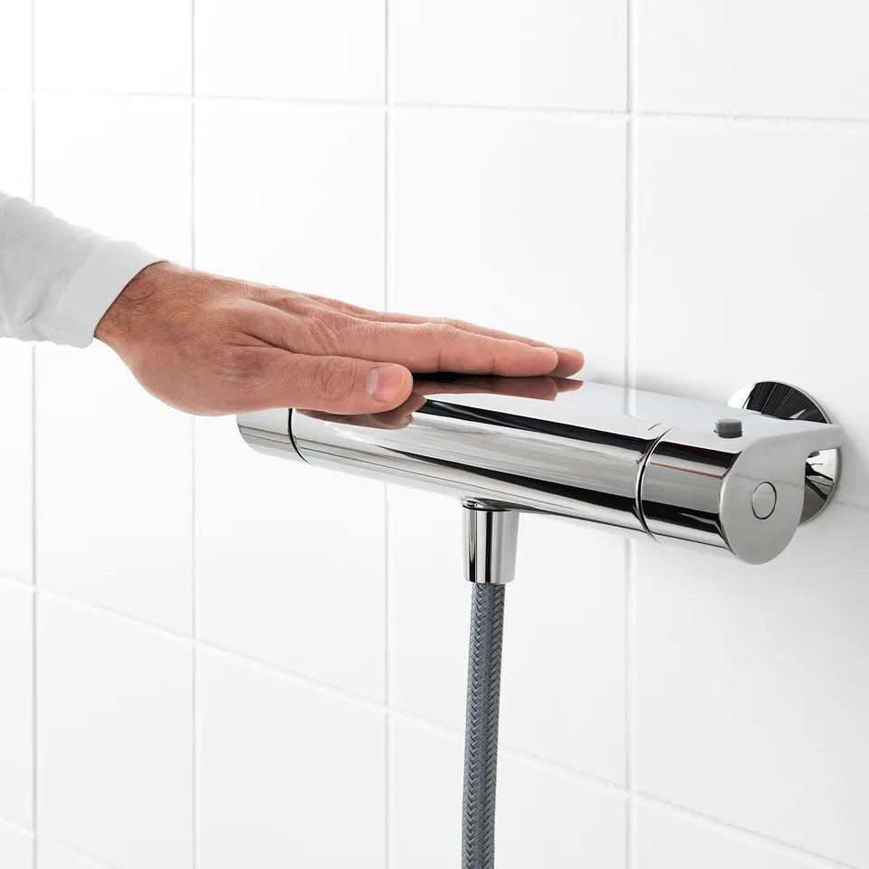A hand adjusts a VALLAMOSSE thermostatic shower mixer, ensuring safe 38°c temperature with cold touch and built-in shelf.