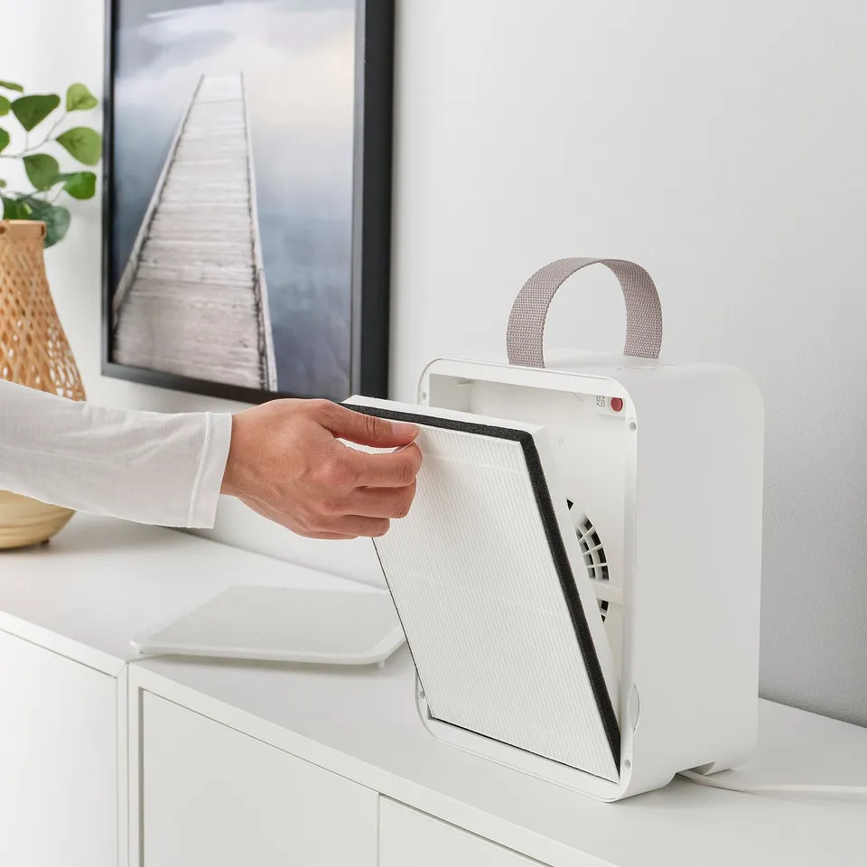 Hand removing philtre from white UPPÅTVIND air purifier on desk.