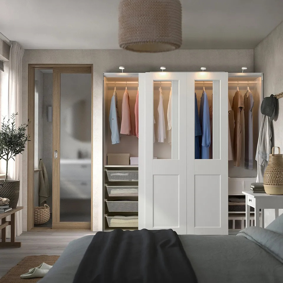 Modern bedroom with white wardrobe, colourful clothes, black bed, and textured light shade.
