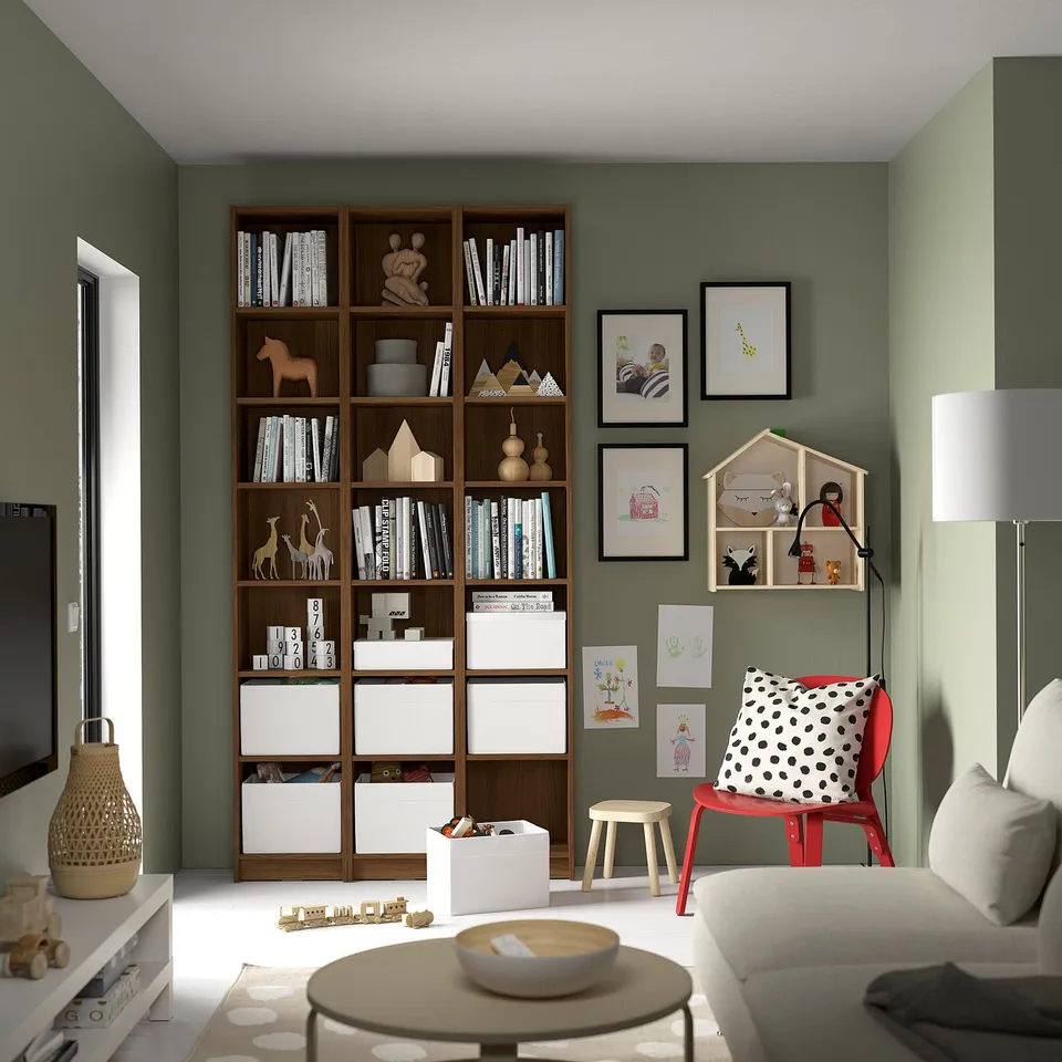 Modern living room with BILLY bookcase, sofa, red chair, coffee table, and dollhouse; green walls.