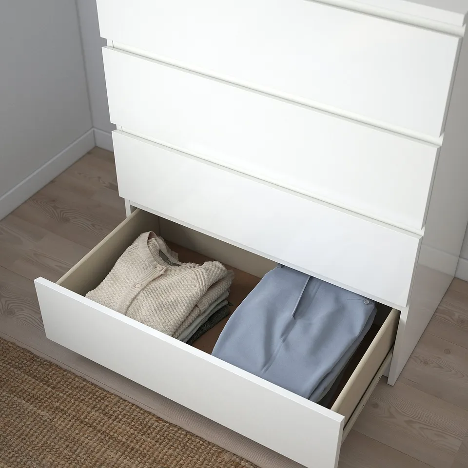 Open white dresser with wood floor, showing tidy clothes in drawers.