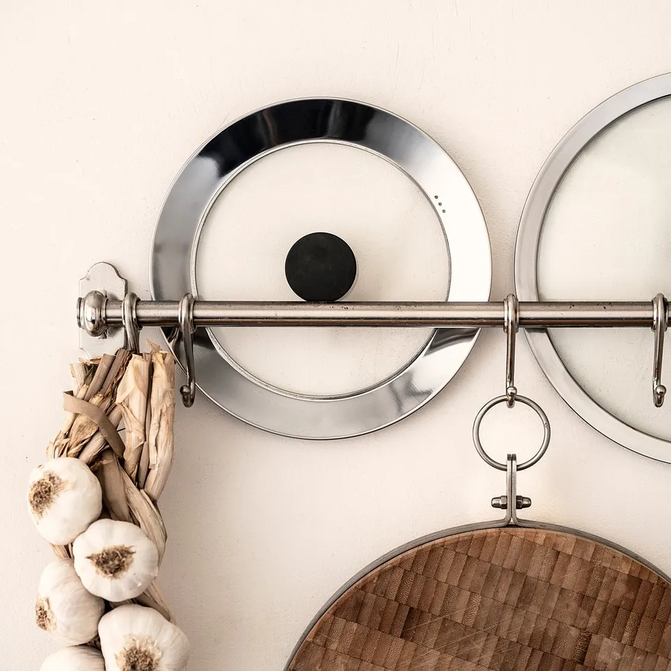 KLOCKREN silver lids hang on wall hooks with garlic bunch, wooden cutting board below.