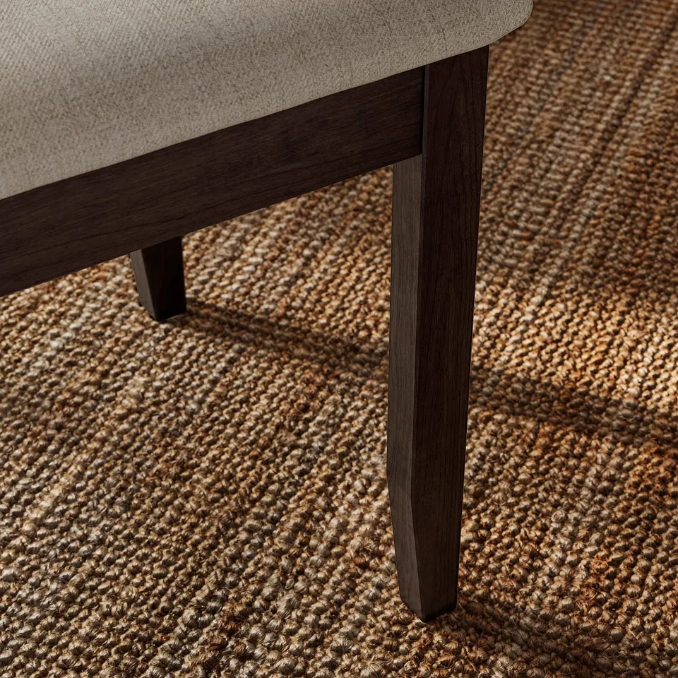 Close-up of sturdy, wooden chair leg, finished with dark stain, supporting comfy, beige upholstered seat on textured, woven rug.