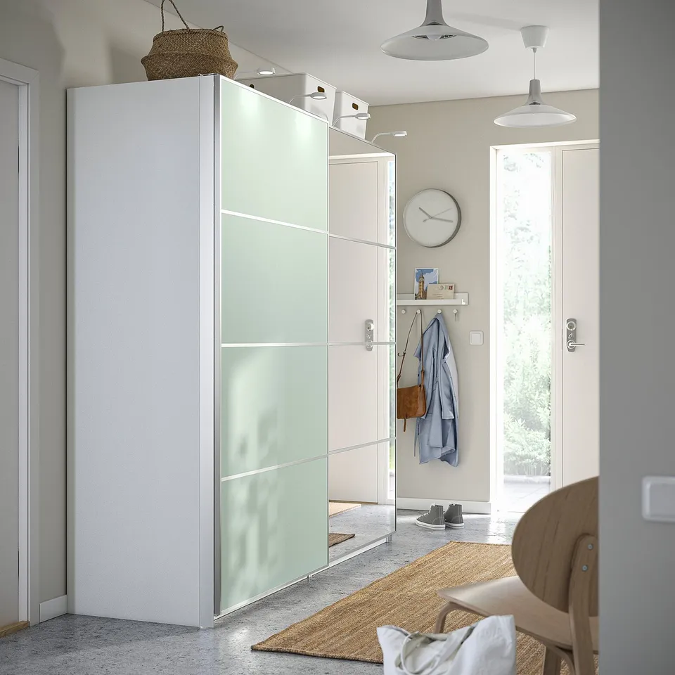 Modern entryway: mirrored sliding door, light chair, beige rug, white decor.