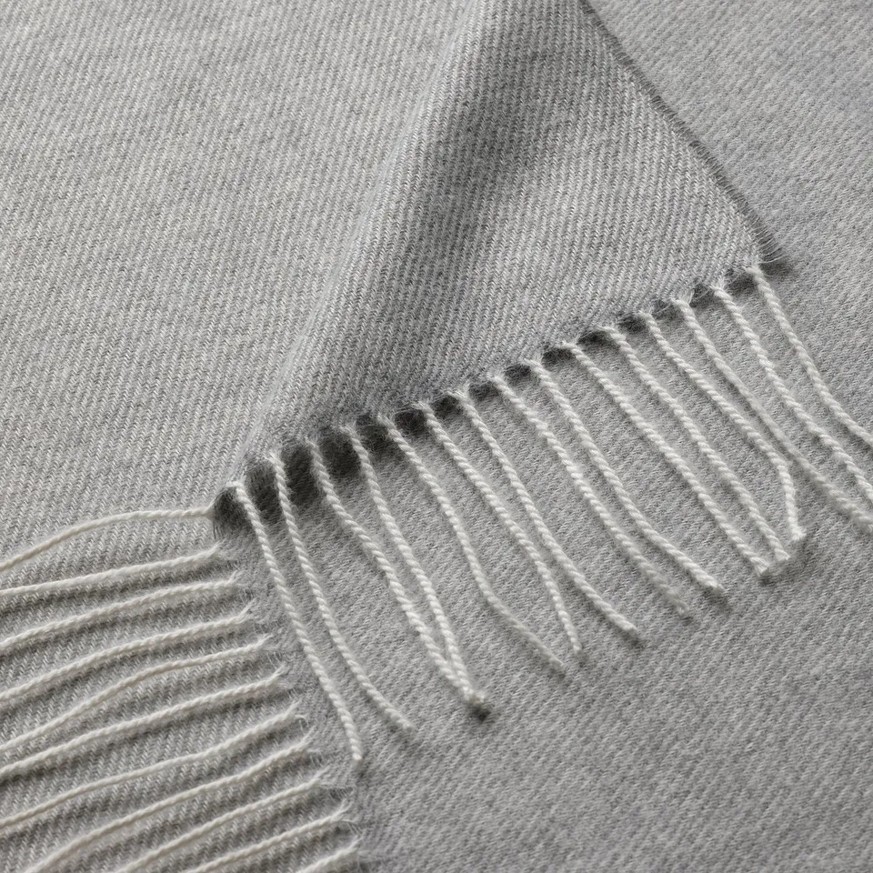Close-up of soft, eco-friendly grey throw with delicate fringes, showcasing high-quality recycled polyester texture.