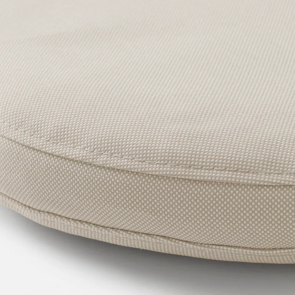 Close-up of round, outdoor cushion cover with neat stitching, soft beige textured fabric, and subtle weave pattern. Zip detail visible.