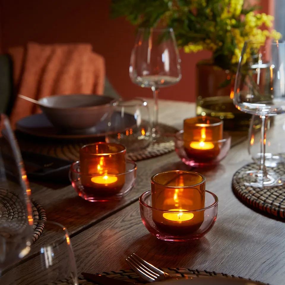Wooden table set with plates, glasses, and lit tealight holders, creating a cosy atmosphere.