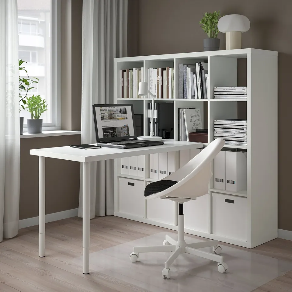 A minimalist home office featuring a white KALLAX shelf with books, a sleek desk, and a bright window.