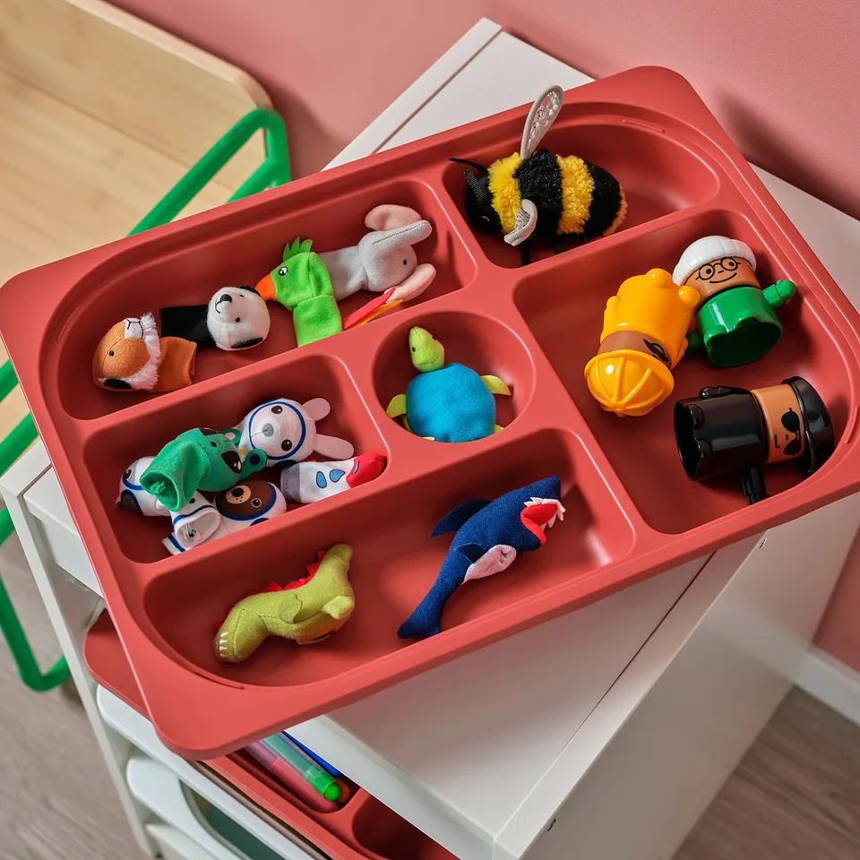 Red TROFAST storage tray with kids toys. Compartments organise stuffed animals, figures, and small items.