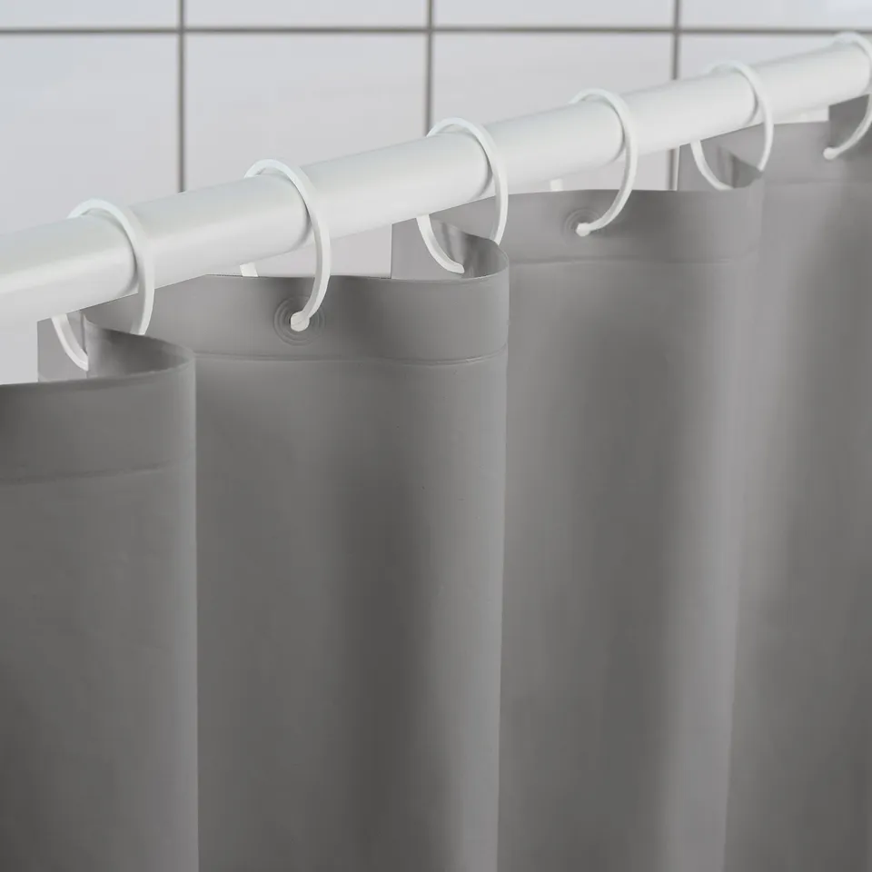 Shower curtain rod with grey, water-repellent curtain and white hooks.