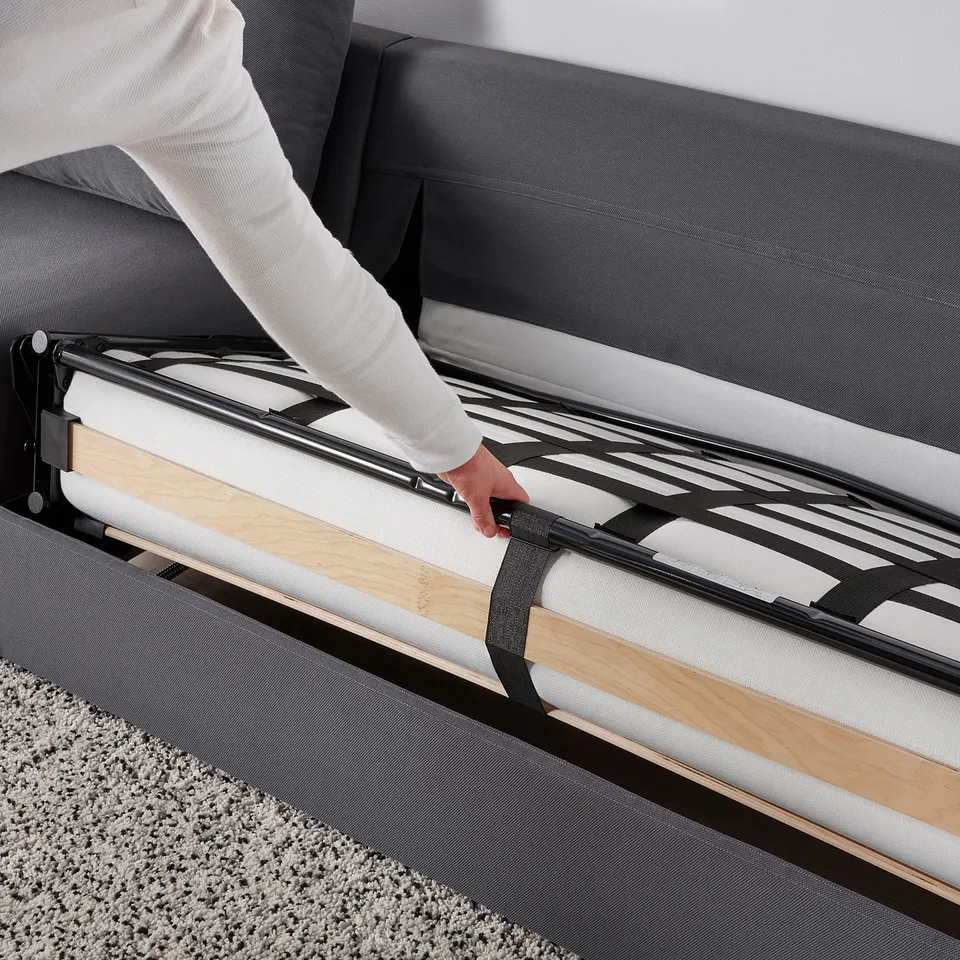 Person adjusts sofa-bed mechanism. Modern sofa converts easily to comfortable bed with thick mattress.