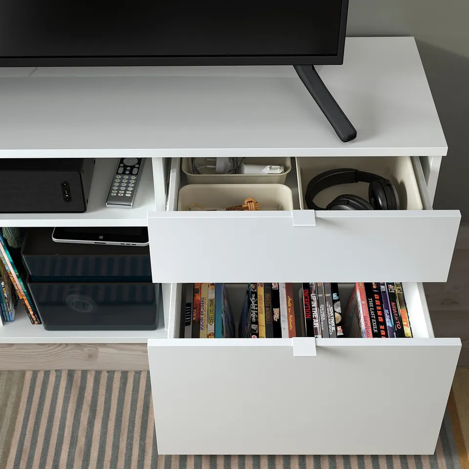 White tv stand with open shelves holding books and media, drawers for storage.