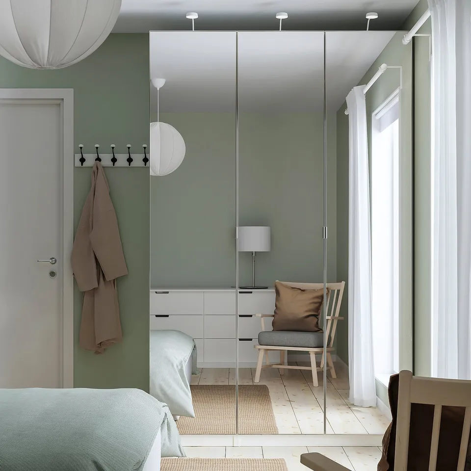 Modern bedroom with mirrored PAX wardrobe, light wood chair, hanging lamps, and light blue decor. Wardrobe tall, chairs compact.