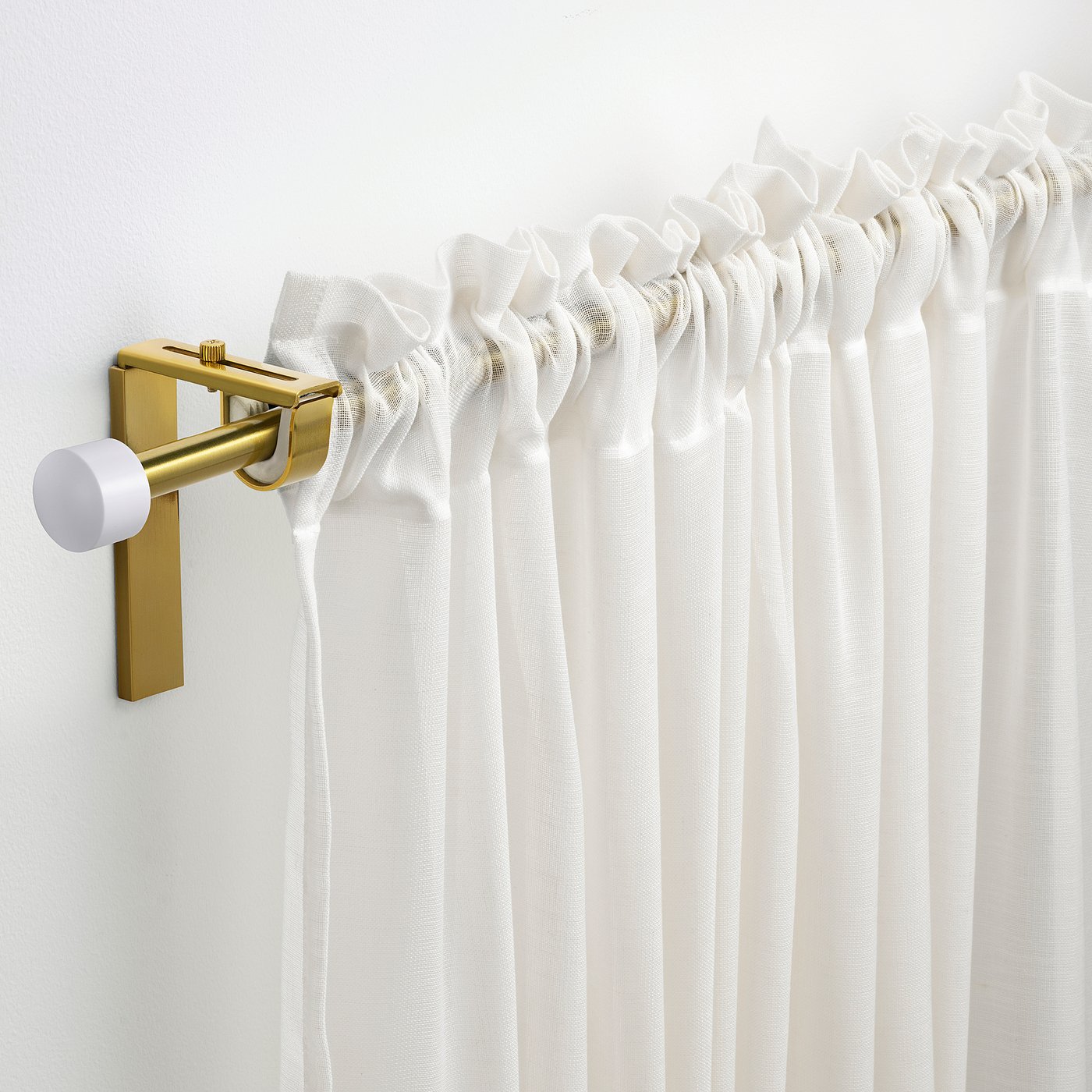 Gold RÄCKA curtain rod with white curtains on light wall.