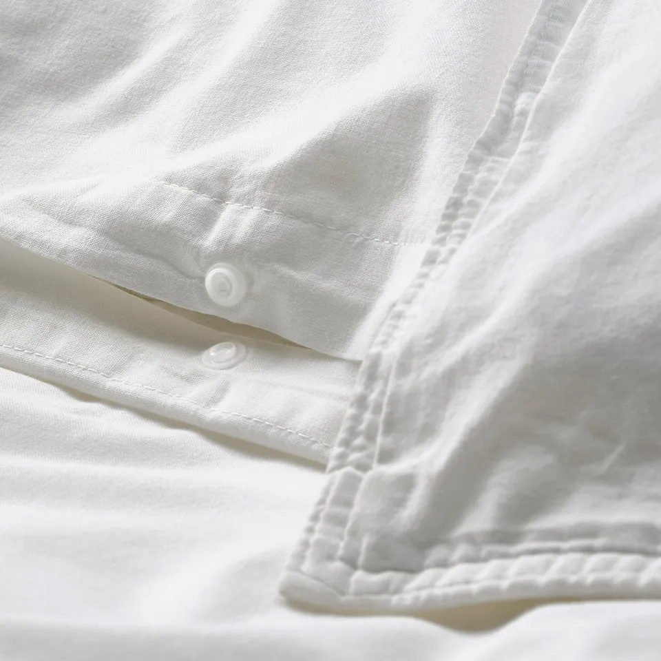 Close-up of white bedsheet with button closure detail. Shows soft, washed cotton texture.