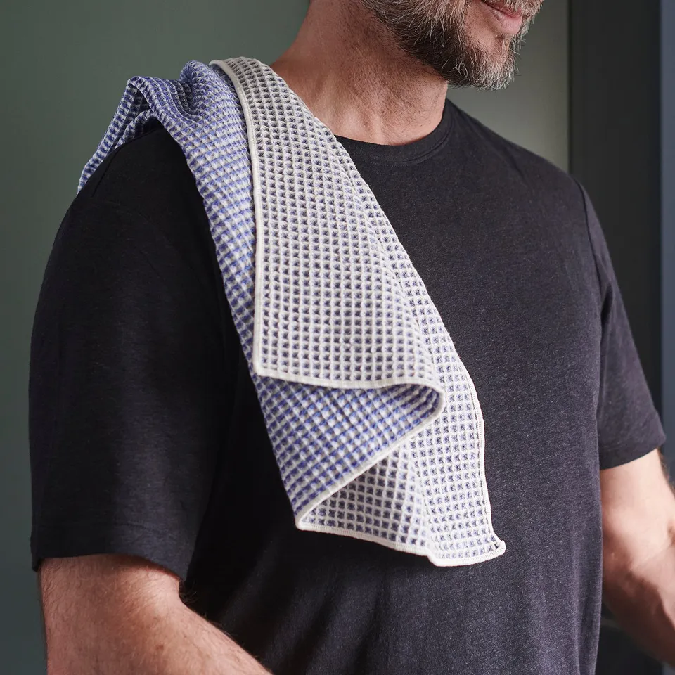 Person holding folded tea towel with waffle texture over shoulder. Towel different patterns on front and back.