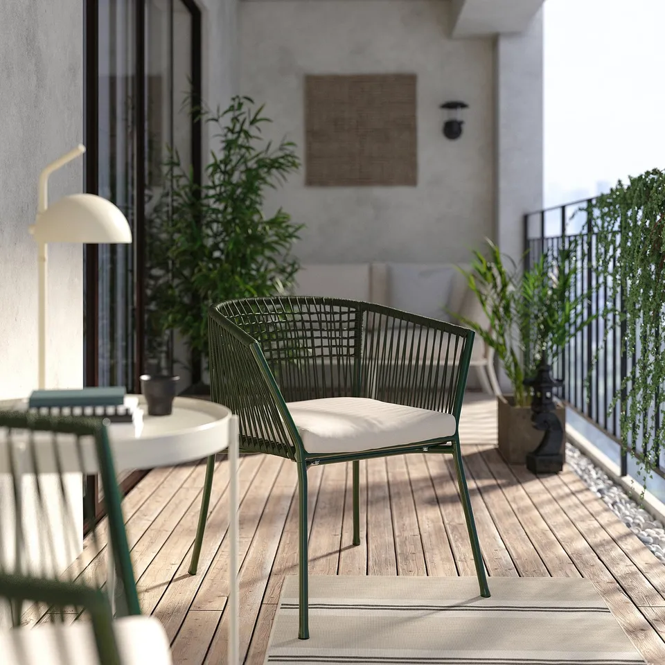Modern balcony setup with SEGERÖN green chair, cushioned seat, black side table, lamp, plants, and woven railing. Relaxing, stylish outdoor space.