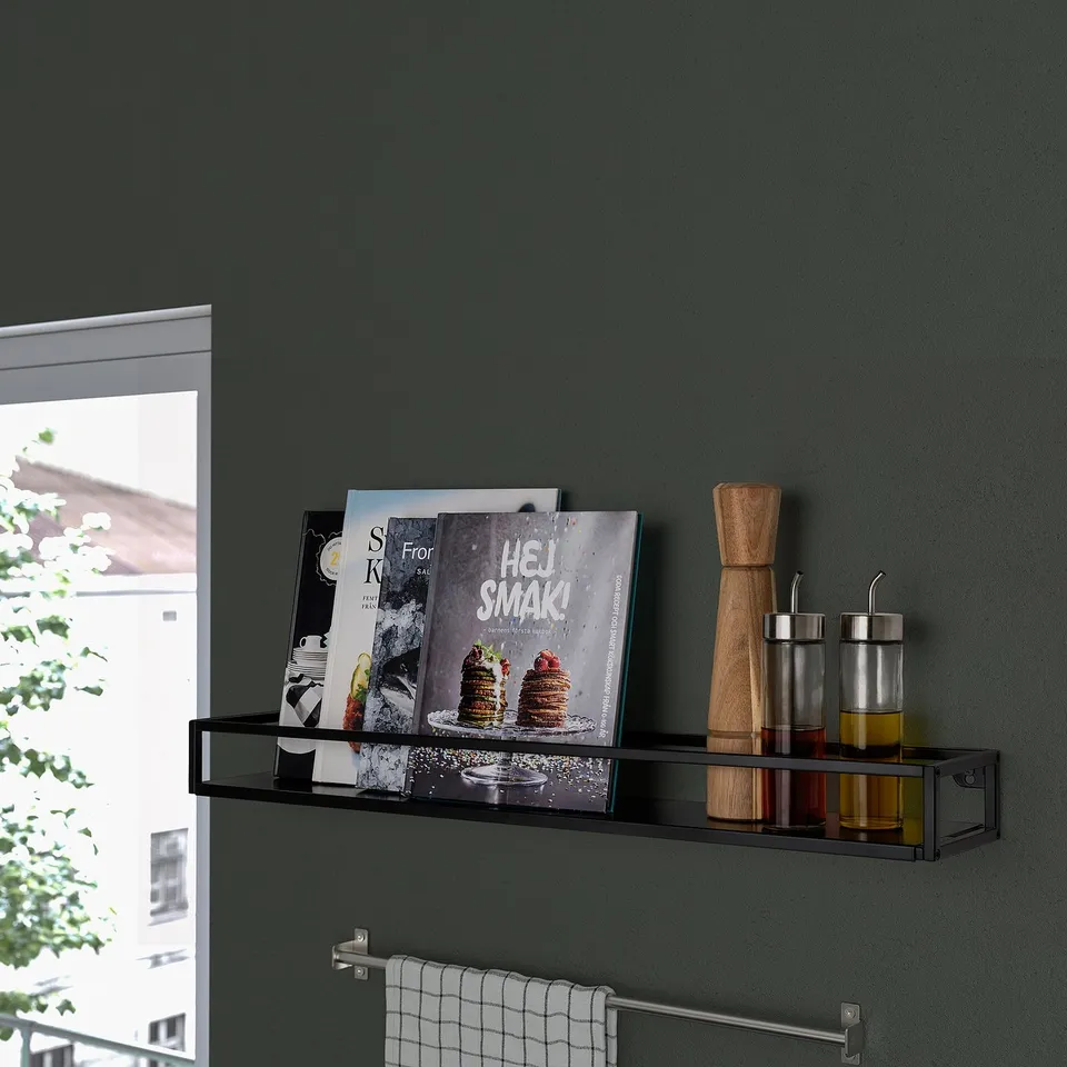 Black modern shelf against green wall, holding cookbooks, wooden utensils, and oil dispensers, near window with plant view.