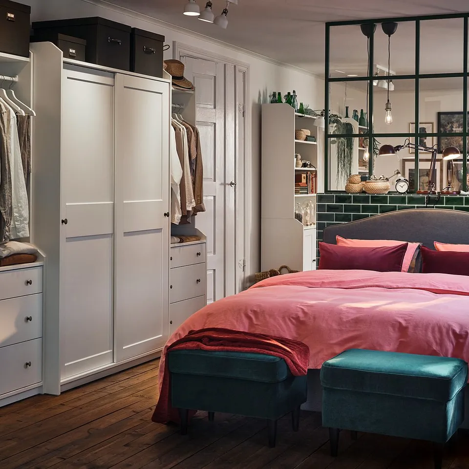 Bright bedroom pink bedding, blue ottomans, and white HAUGA wardrobes with sliding doors. Modern decor with wood floors.