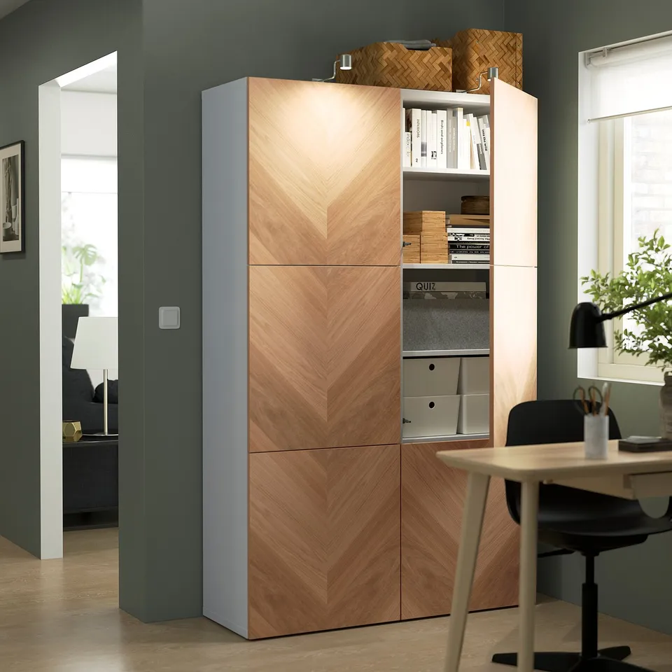 Wooden storage unit with open shelves holding books and boxes, standing in a home office near a desk with a computer and plants.