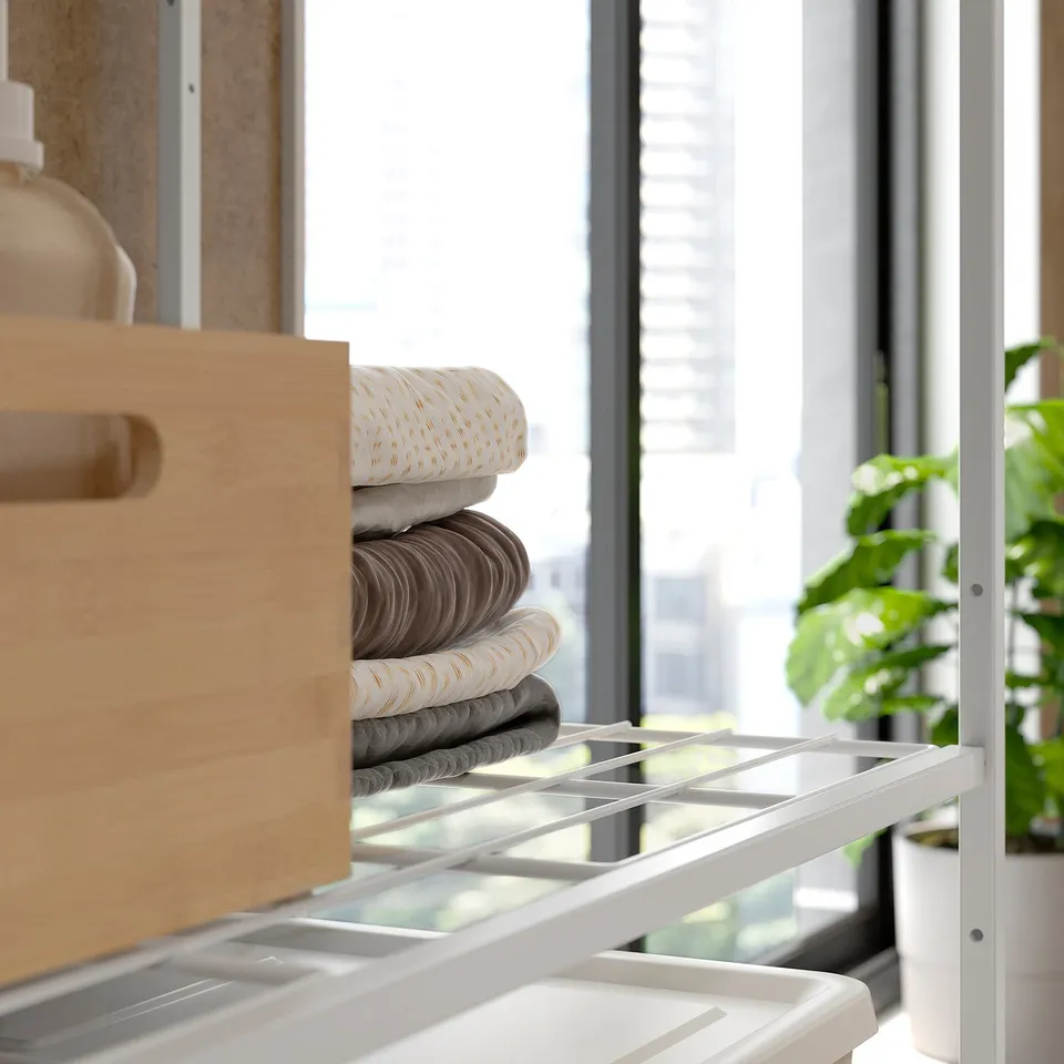 White JOSTEIN metal shelving unit with fabric folds and wooden drawer near window.