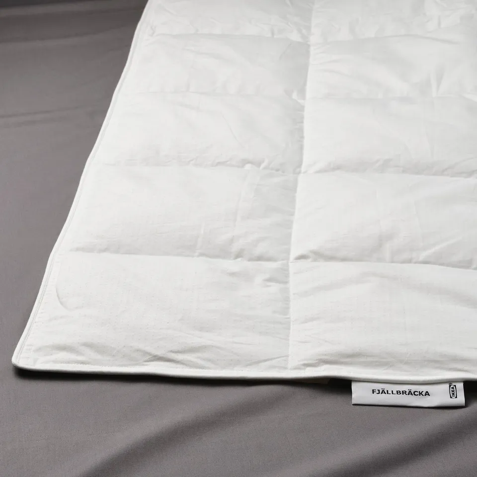 Lightweight duvet with box-stitch pattern, lying on grey bedding, with FJÄLLBRÄCKA label visible.