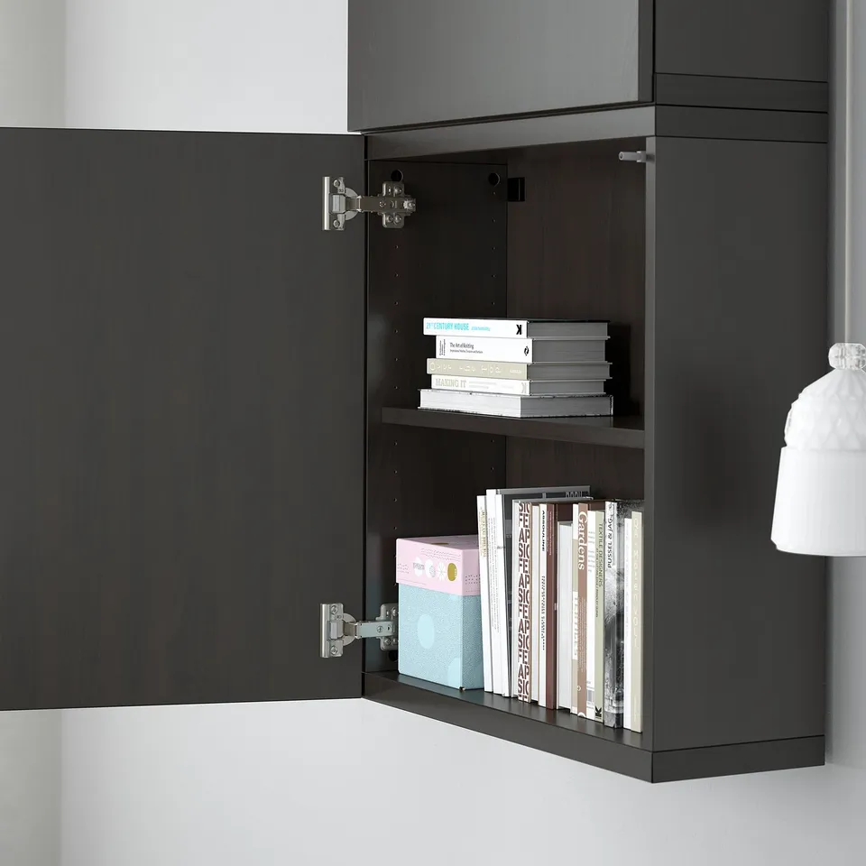 Black wall-mounted cabinet with open door, revealing two shelves stacked with various books and a box. Suspended from a metallic rail.
