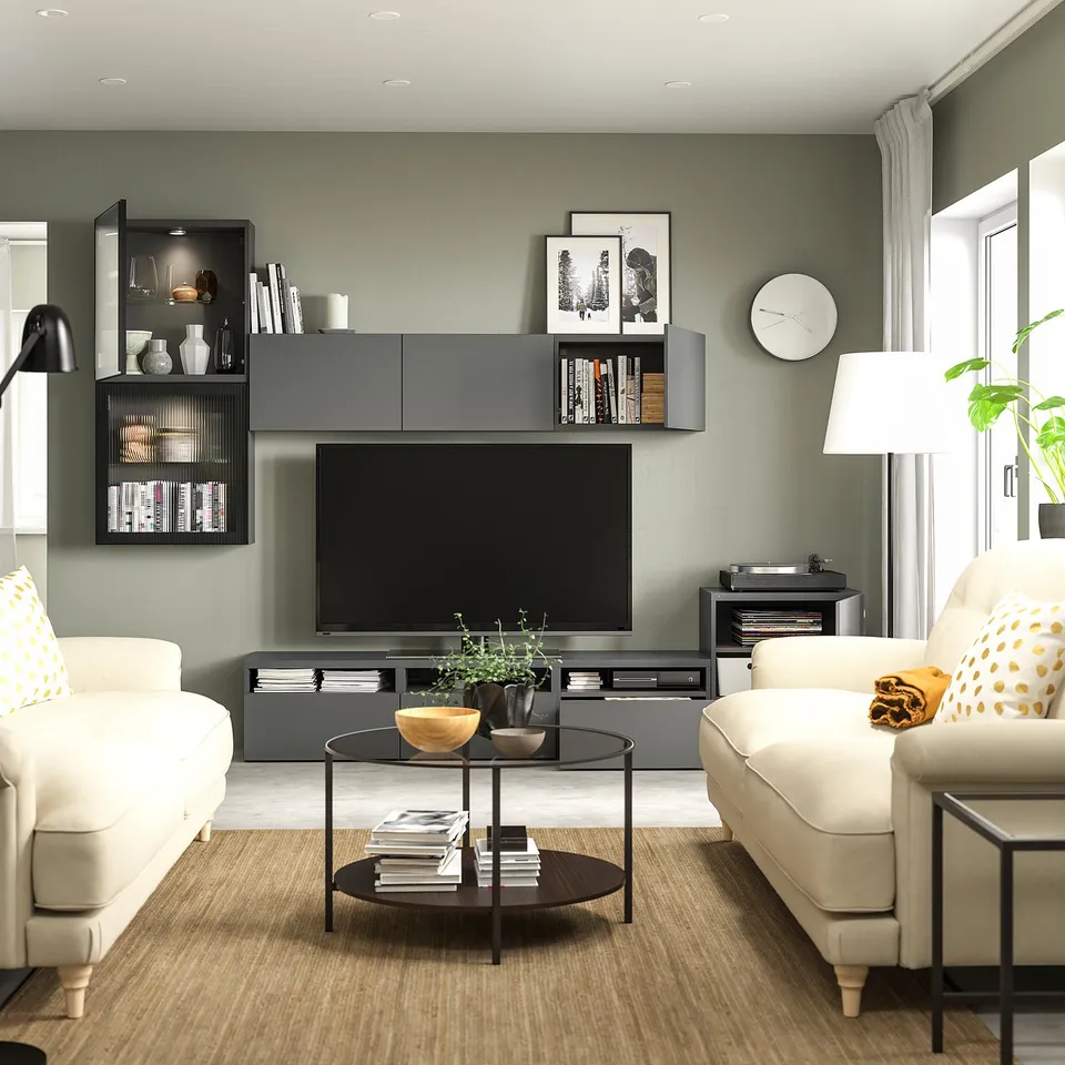 Modern living room with light beige sofas, black and grey tv unit, flat-screen tv, circular coffee table, and green painted walls.