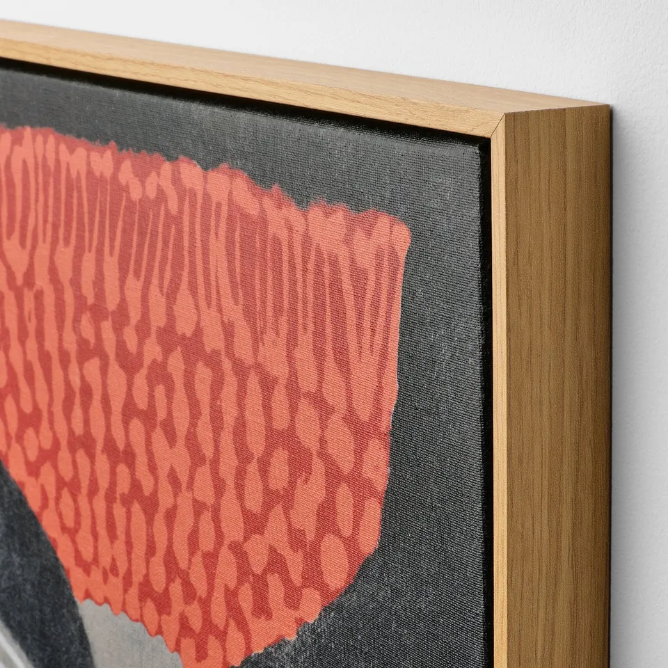 Close-up of framed canvas artwork. Intricate red pattern on dark background. Oak effect frame enhances quality.