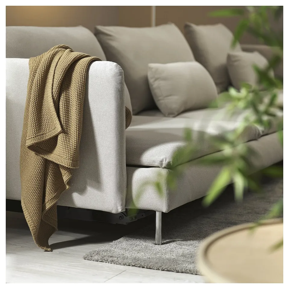 Modern beige sofa bed with metal legs, displayed with pillows, blanket, and plant.