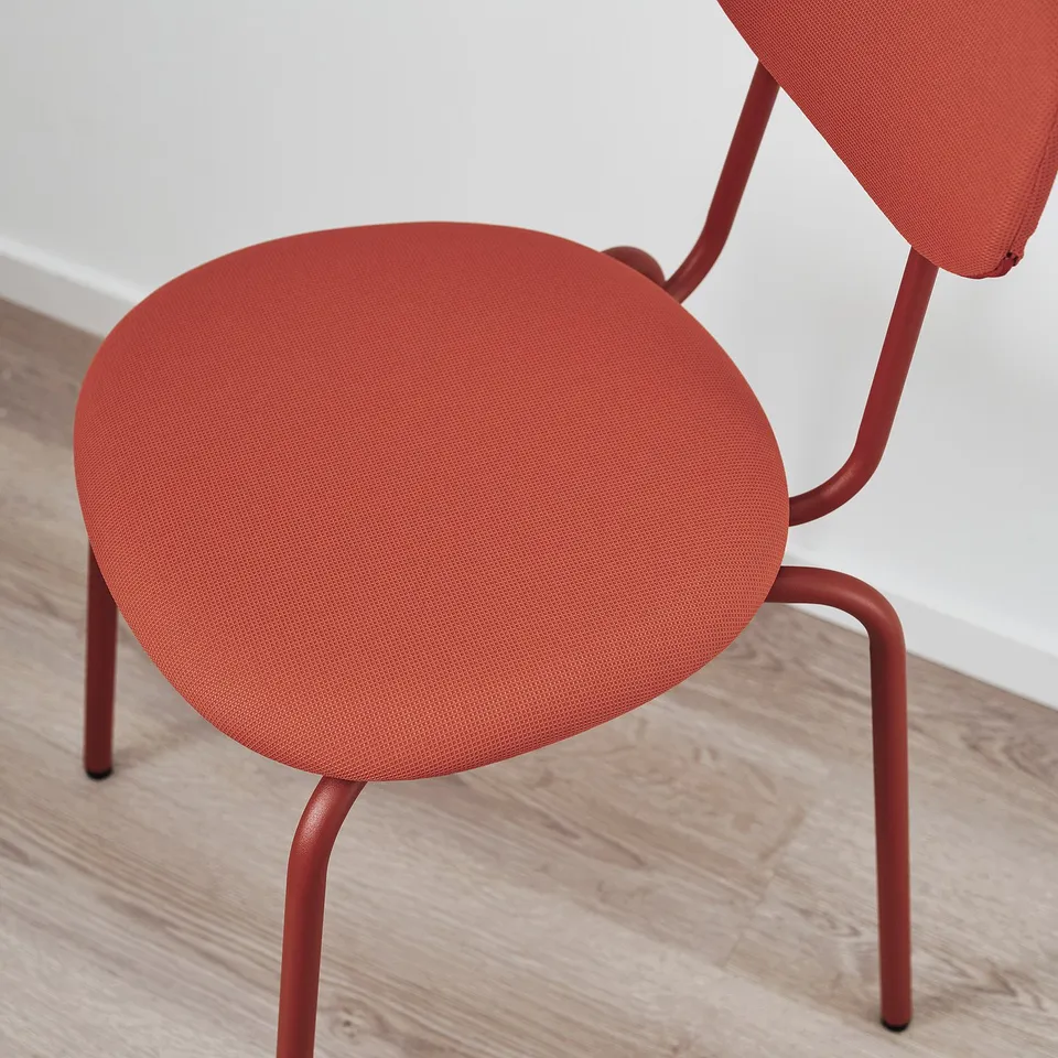 Red modern chair with curved legs, sleek design, vibrant colour, placed near white wall.