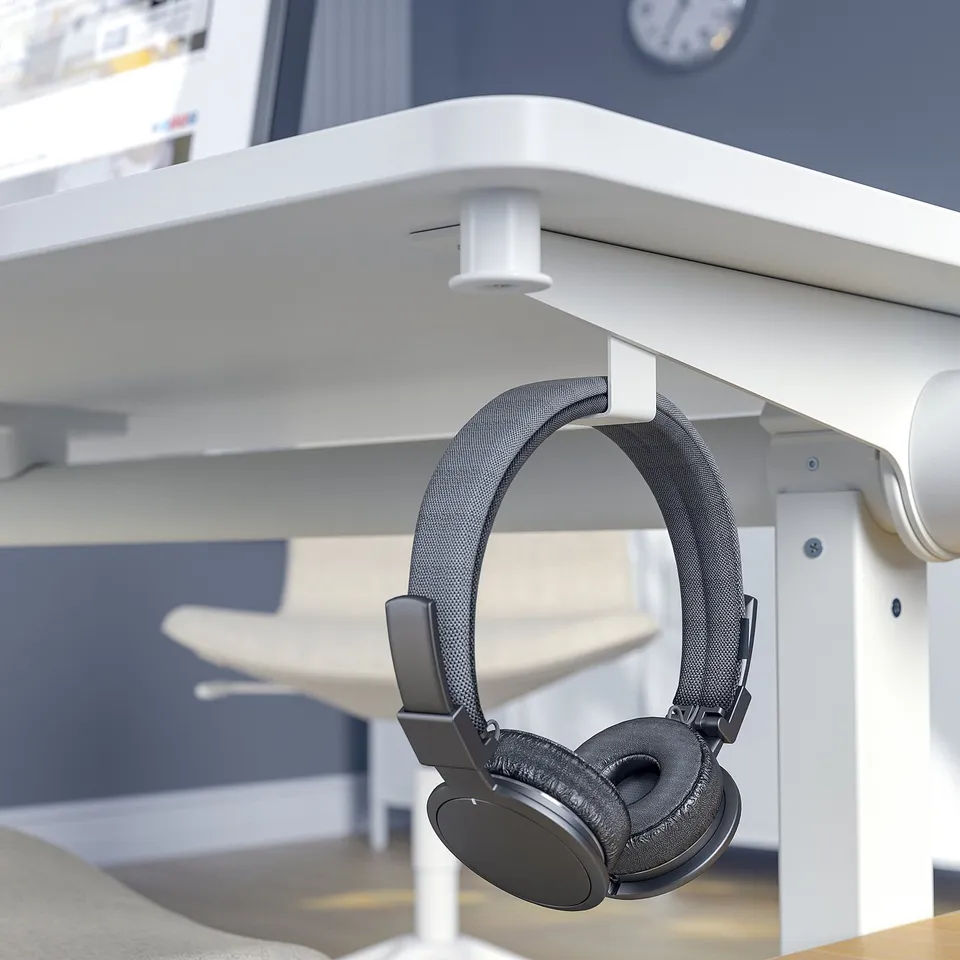 Black headphones hang on white table hook, ideal for meeting rooms.