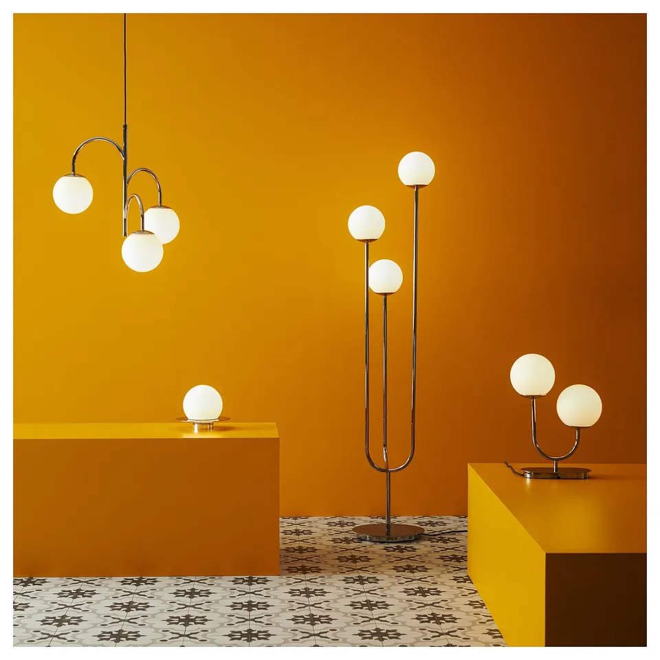 Modern room with yellow walls, geometric floor tiles, and sleek lamps. Four spherical, chrome-lit lamps hang, stand, and sit, casting soft light.