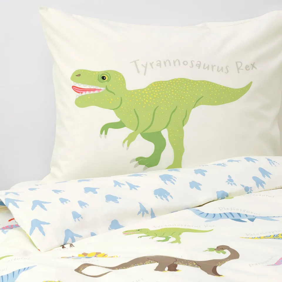 Cartoon dinosaur on green pillow, marked tyrannosaurus rex. Soft bedding with assorted dinosaur prints.
